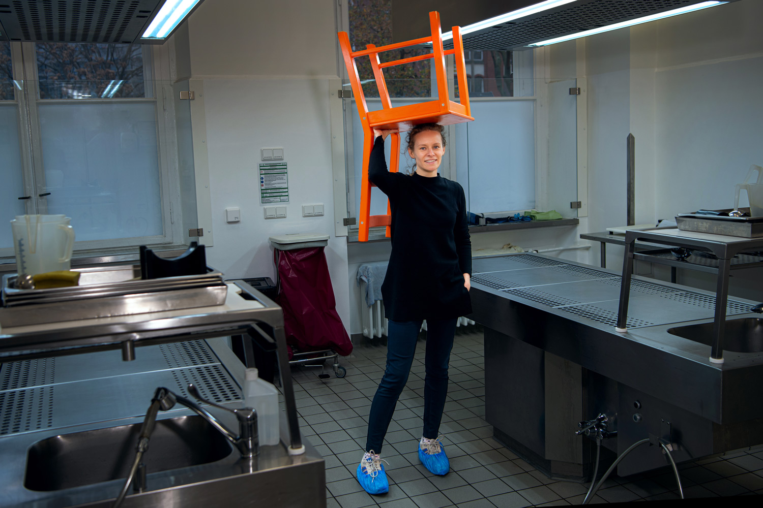 .Josefine Rdake tägt einen orangefarbenen Stuhl auf ihrem Kopf in der Pathologie auf dem Campus MItte