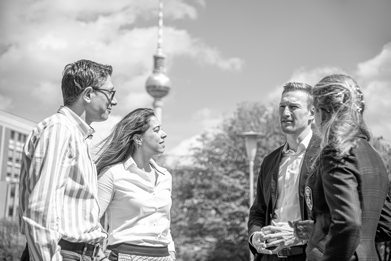 vier Studierende unterhalten sich im Freien im Sommer, im Hintergrund der fernsehturm