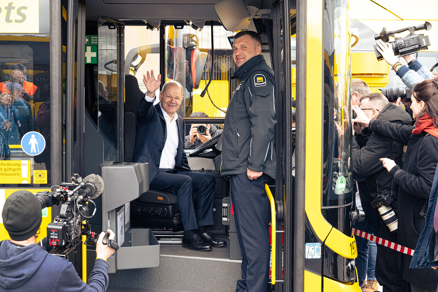 Bundeskanzler Olaf Scholz sitzt winkend in einem Bus der Berliner Verkehrsgesellschaft, BVG